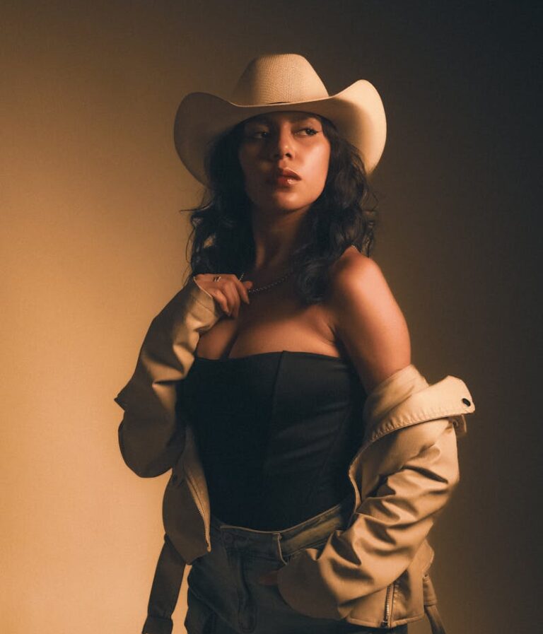 Chic woman in cowboy hat poses with confidence under warm lighting.
